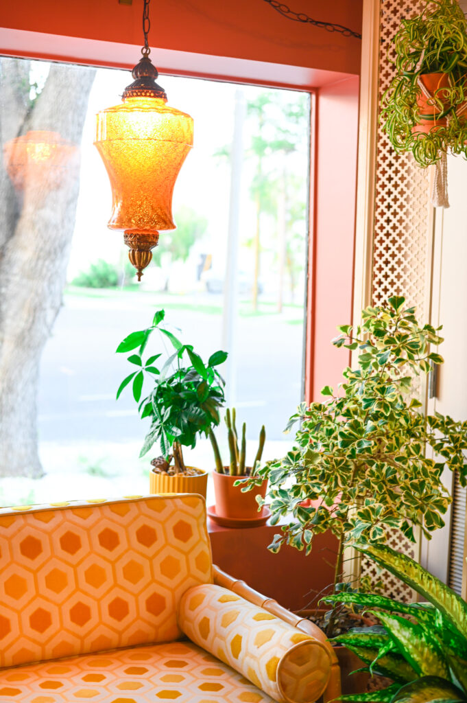 Cozy seating area with orange patterned furniture, amber pendant lighting, and green plants, styled for Florida restaurant or hotel branding
